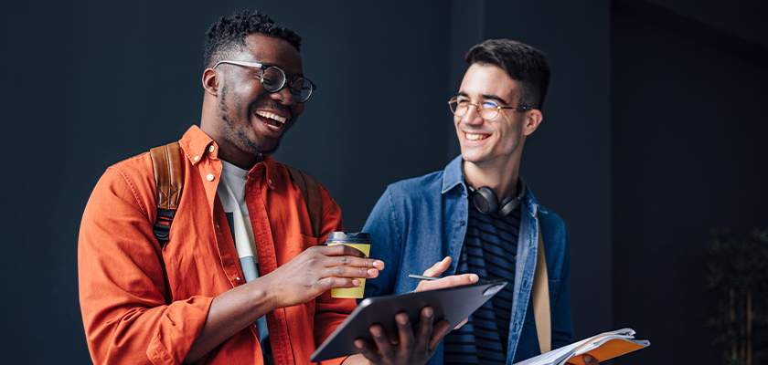 2 male students reviewing school work on tablet while laughing with one another