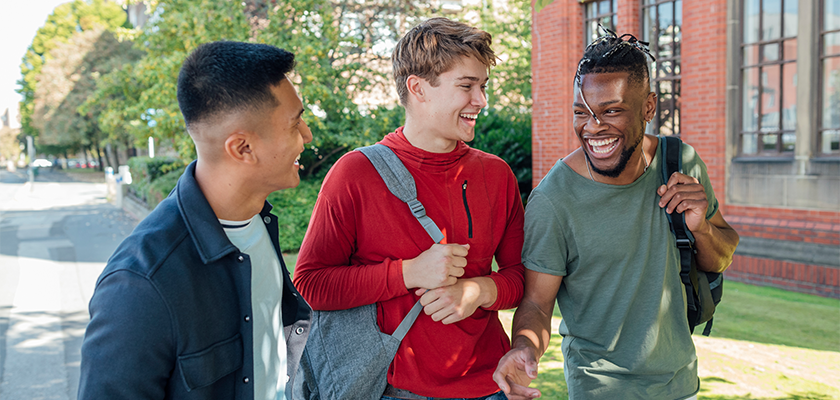 3 male students walking on campus laughing together