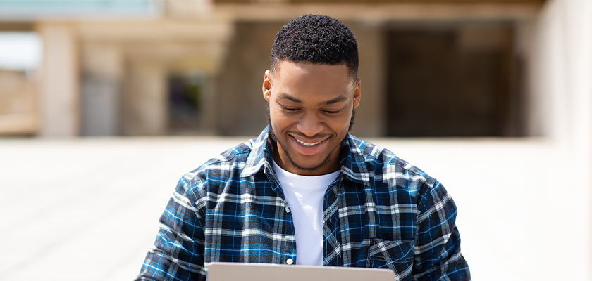 Male student doing school work on laptop while smiling