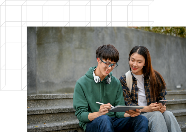 Two students sit on outdoor steps, one holding a tablet and stylus while the other watches, smiling. They appear to be studying or collaborating on a project.